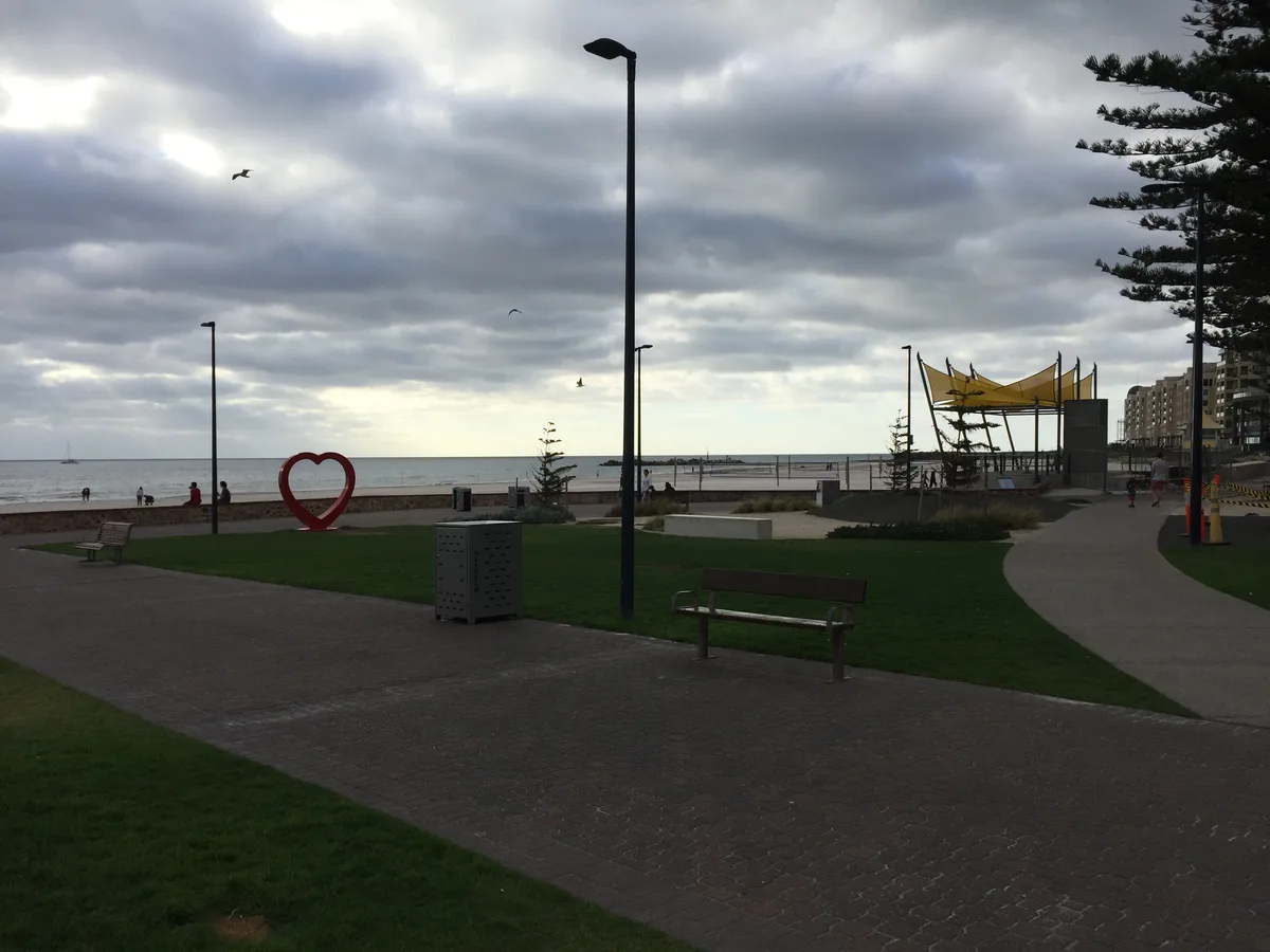グレネルグの海辺の遊歩道。芝生の上に赤いハートのモニュメント、空にはカモメ、奥に浜辺と海が広がる